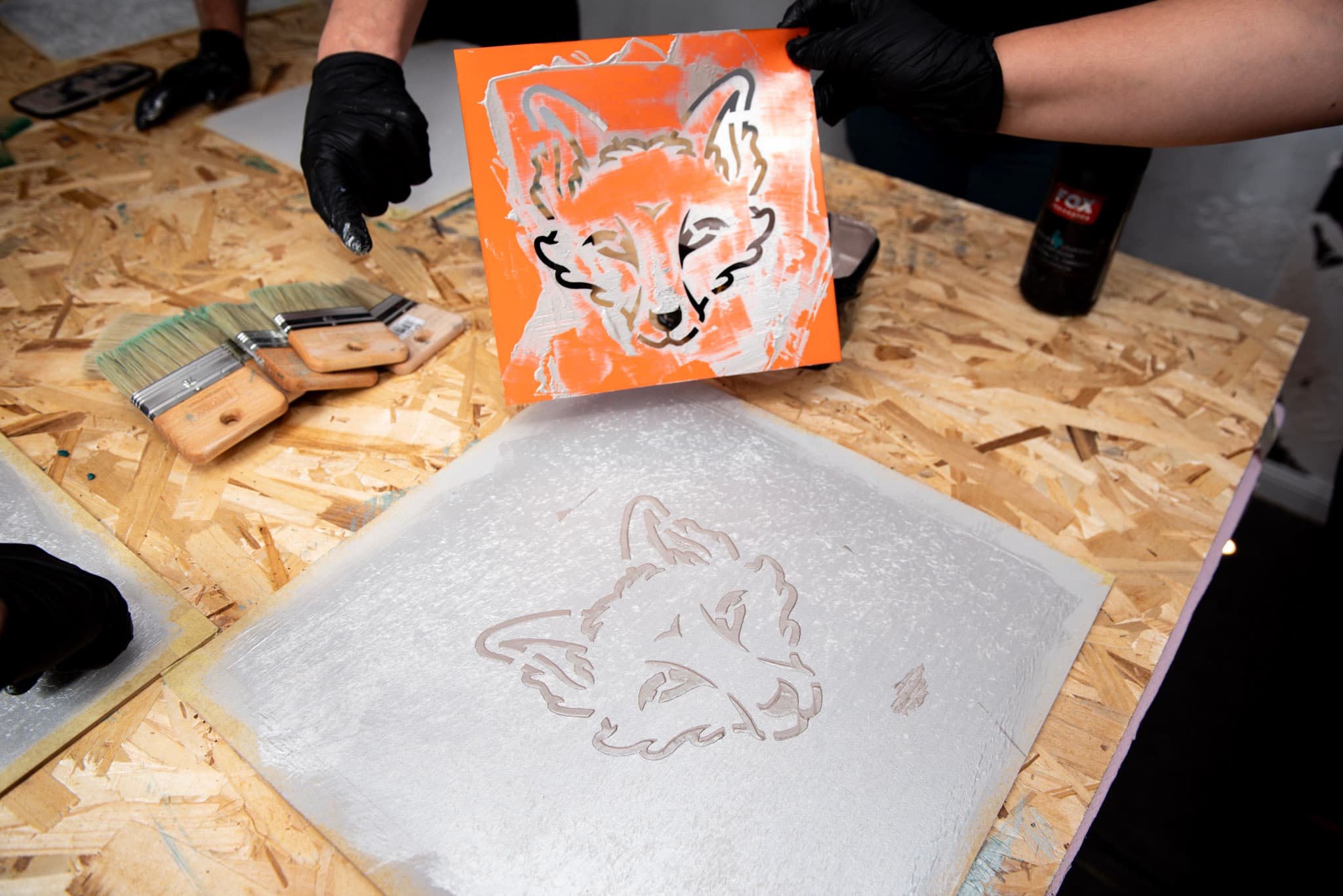 Applying a decorative stencil to a sample board, with brushes and Fox Dekorator products on the workbench