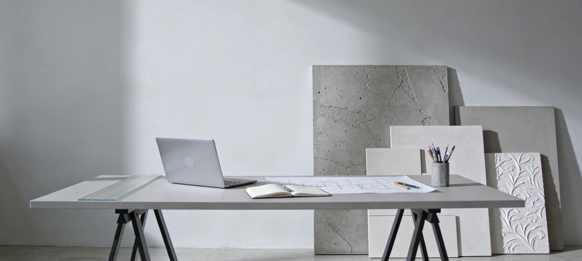 An architecture desk with drawings, a laptop and decorative plaster sample boards leaning against the wall